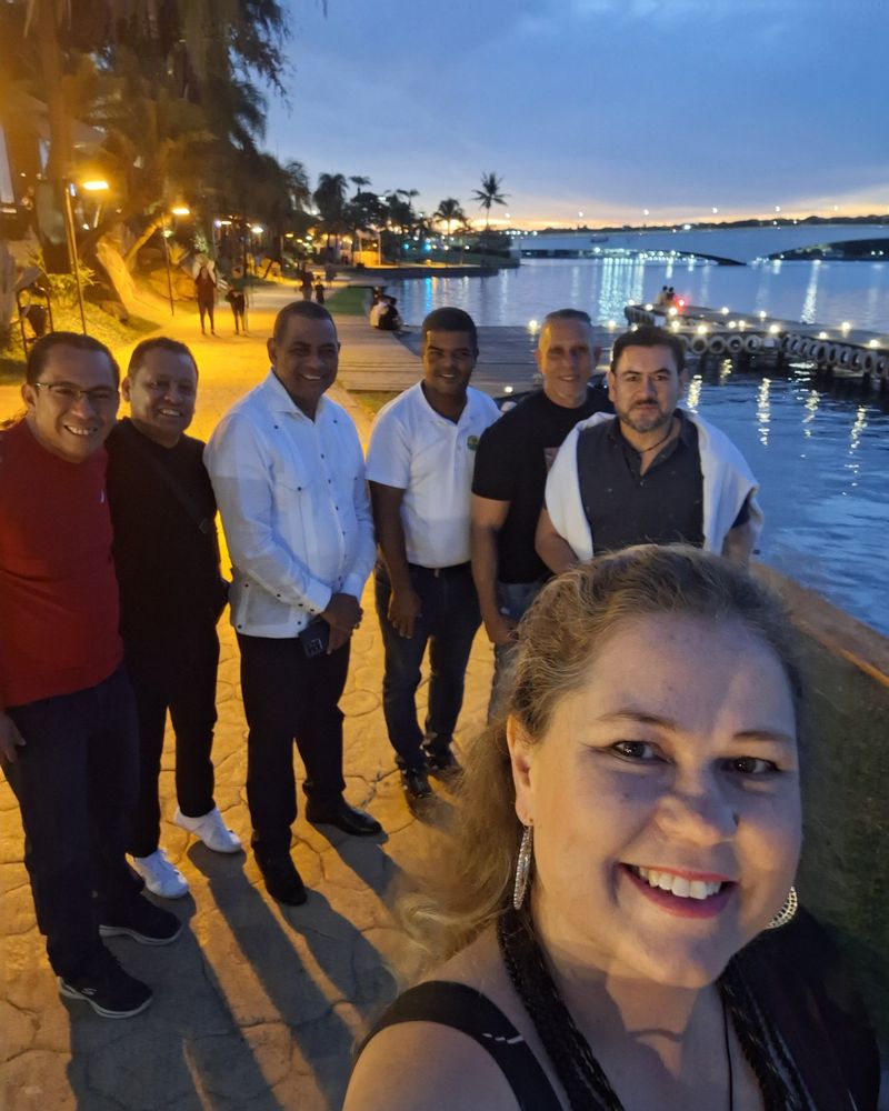 Andressa Wildner em selfie com um grupo de viajantes à beira de um lago ao entardecer